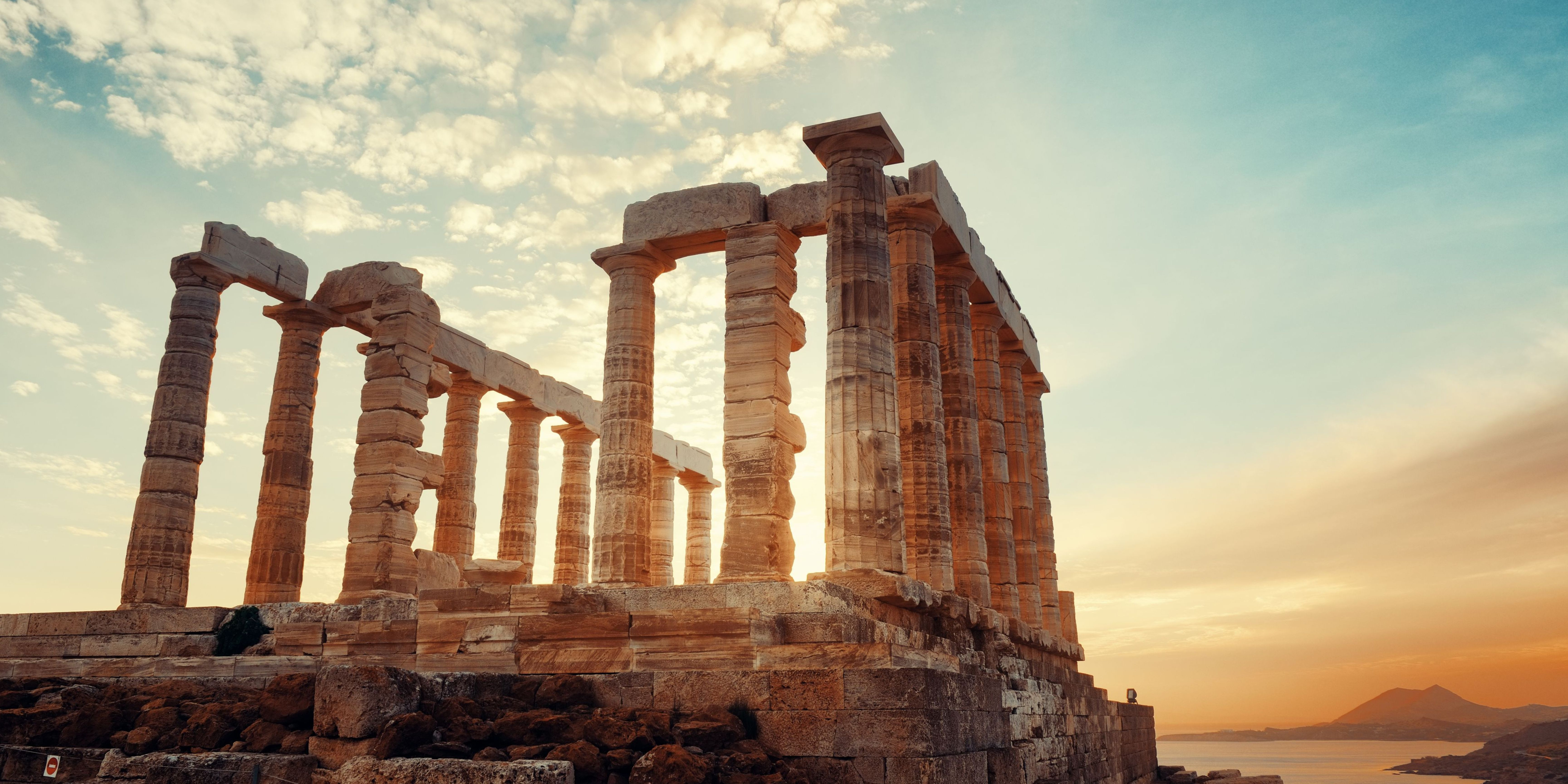 Sunset view of the Temple of Poseidon ruins with the sea in the background.
